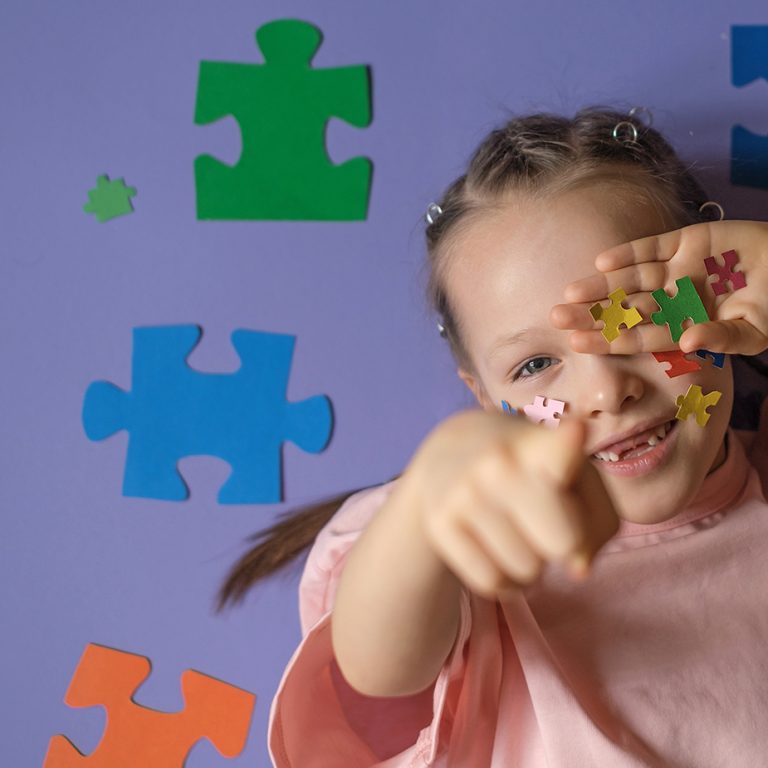 A girl with a lot of pieces of colorful puzzles in hand points finger forward. Banner on education and awareness about autism