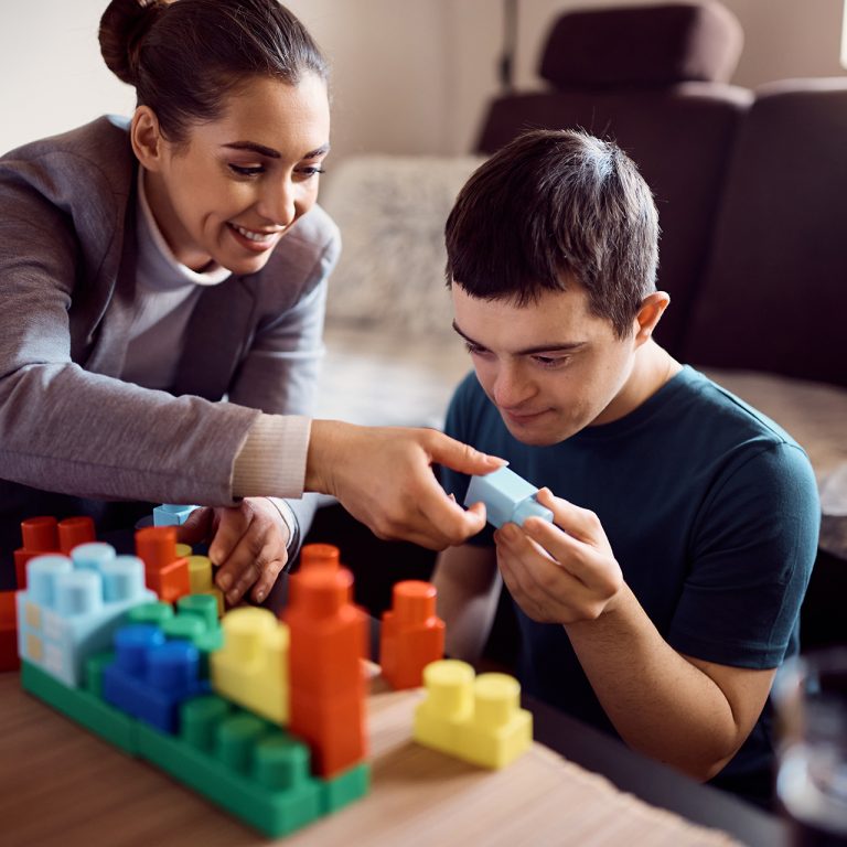 Happy psychologist and man who has down syndrome playing with toy blocks during home visit.